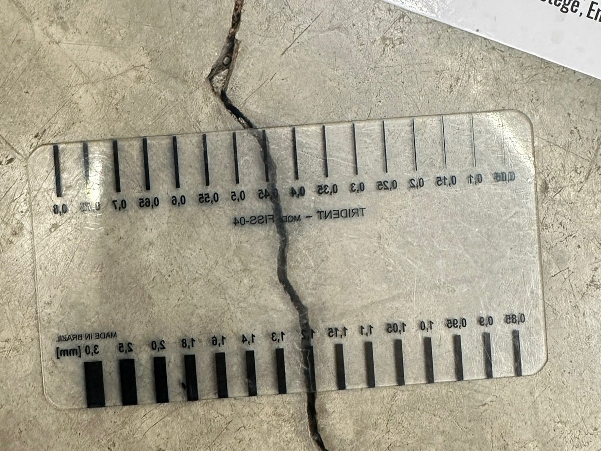 Fissurômetro posicionado sobre trinca em piso de concreto para medir a abertura